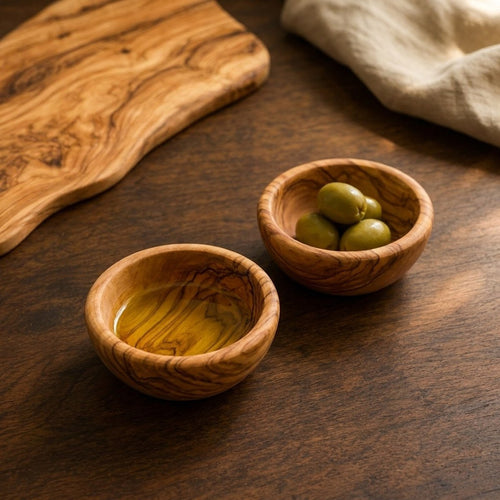 The two olive wood dip bowls on an olive wood board with oil and olives